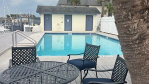 A pool area with a table and chairs, a building with doors, and a palm tree. - The Moorings Hotel and Marina  (Carrabelle)