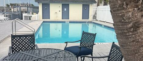 A pool area with a table and chairs, a building with doors, and a palm tree.