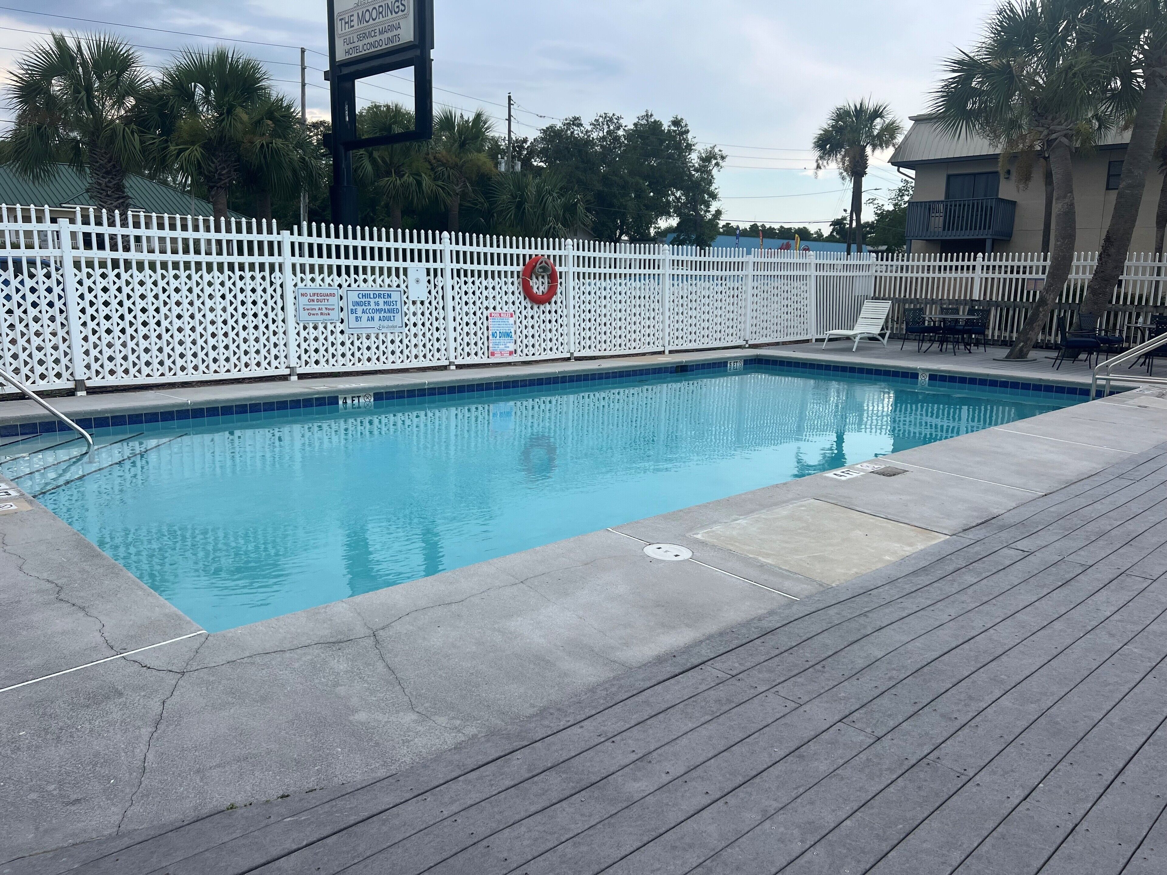 Une piscine entourée d’une clôture blanche, avec un poste de surveillance pour les sauveteurs et un panneau indiquant qu’elle fait partie du complexe hôtelier et des résidences de la marina The Moorings, qui offre tous les services.