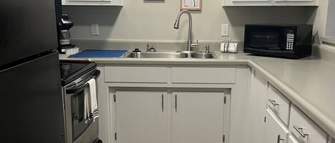 A kitchen with white cabinets, a stainless steel refrigerator, a microwave, and a sink.