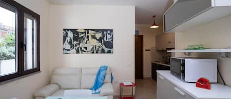 A compact kitchen with a dining area, a sofa, and a painting on the wall.