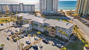 Un hotel su più piani con un parcheggio, circondato da palme e vista sulla spiaggia.