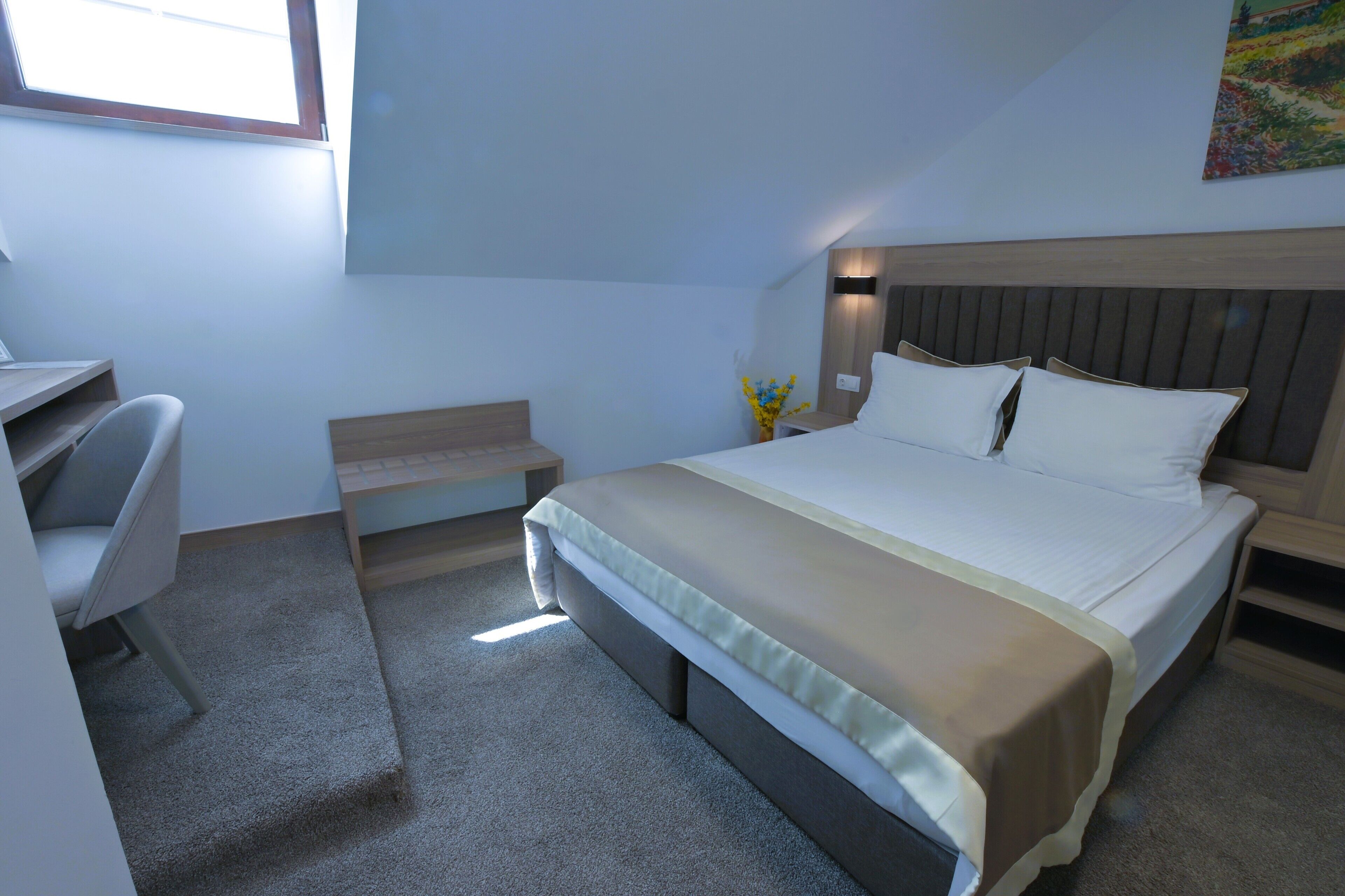A bedroom with a bed, desk, chair, and a small table with a vase of flowers.