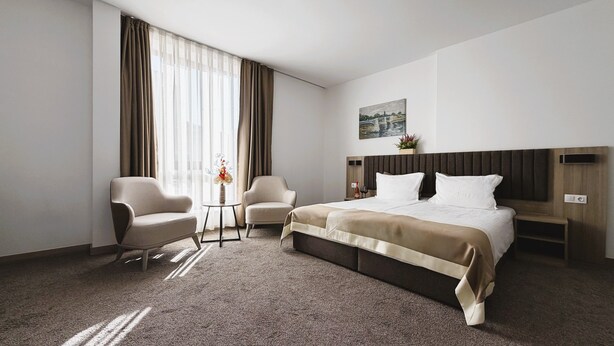 Habitación de hotel con cama, dos sillones, una mesita con un jarrón y un cuadro en la pared.