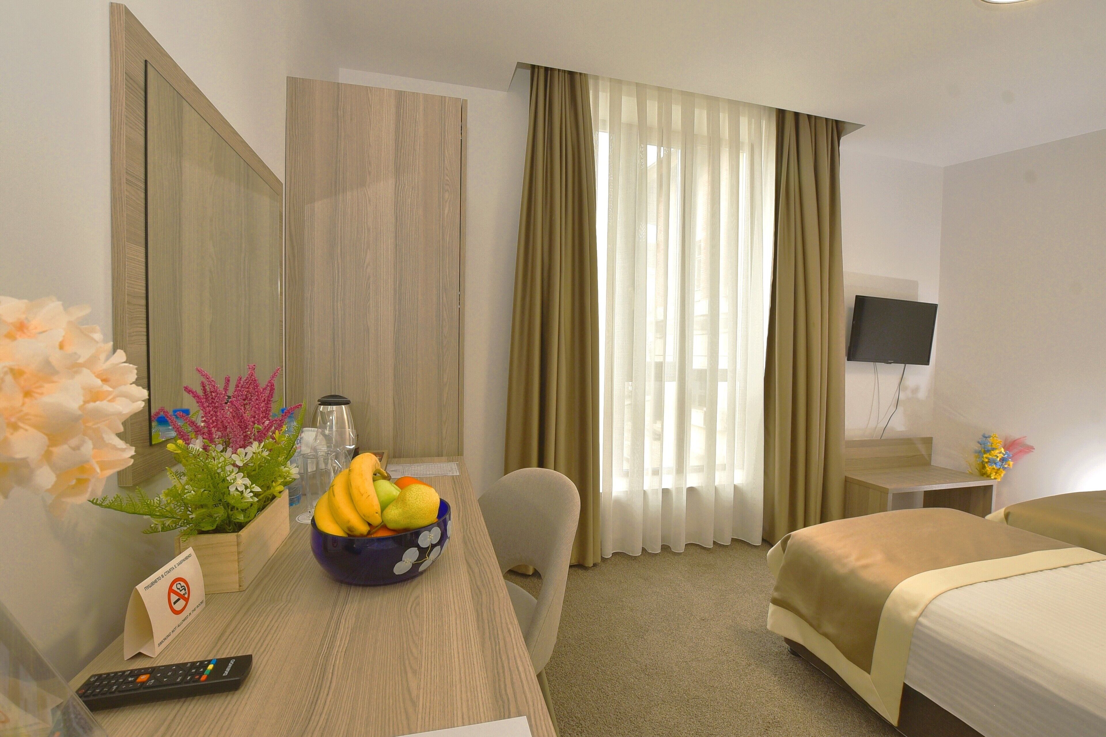 A hotel room with a bed, a desk with a bowl of fruit, a remote control, and a television.