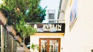 Un edificio llamado 'EVELIN' con una escalera que conduce a la entrada, asientos exteriores con sillas y mesas, y una planta en maceta.