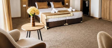 Habitación de hotel con cama, dos sillas, una mesita con un jarrón y un cuadro en la pared.