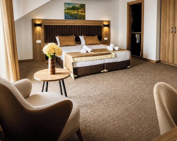 A hotel room with a bed, two chairs, a small table with a vase, and a painting on the wall. - Evelin Deluxe House (Plovdiv)