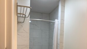 Une salle de bain avec un lavabo blanc, un rideau de douche et un mur recouvert de carreaux de marbre.