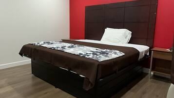 A bedroom with a bed, a nightstand, and a red accent wall.