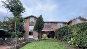 A two-story house with a brick exterior, a well-maintained lawn, and various potted plants. - Captivating 3-bed House in Kigali , Rwanda (Kigali)