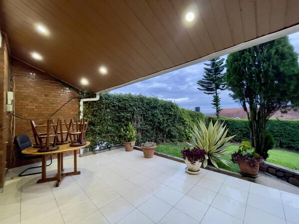 A covered patio with a wooden ceiling, a brick wall, and a view of a green landscape. - Captivating 3-bed House in Kigali , Rwanda (Kigali)