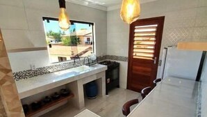 A kitchen with a marble countertop, a sink, a window, and a door with blinds. - Harmonia Flats (Tibau do Sul)