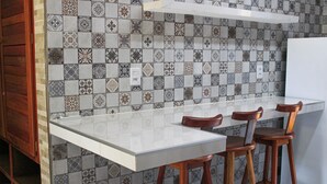 A kitchen with a tiled backsplash, a white countertop, and wooden bar stools. - Harmonia Flats (Tibau do Sul)