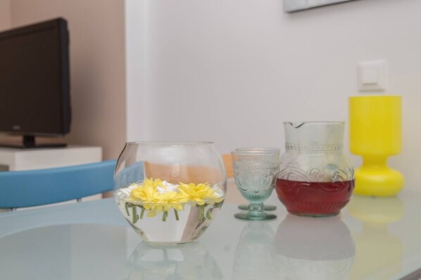 Une table sur laquelle se trouvent un vase en verre contenant des fleurs jaunes, une carafe en verre remplie d’un liquide rouge et une bouteille jaune.