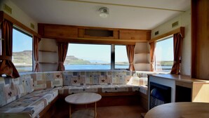 A cozy RV interior with a large window offering a scenic view, a cushioned seating area, and a small table. - Canna Campsite (Isle of Canna)