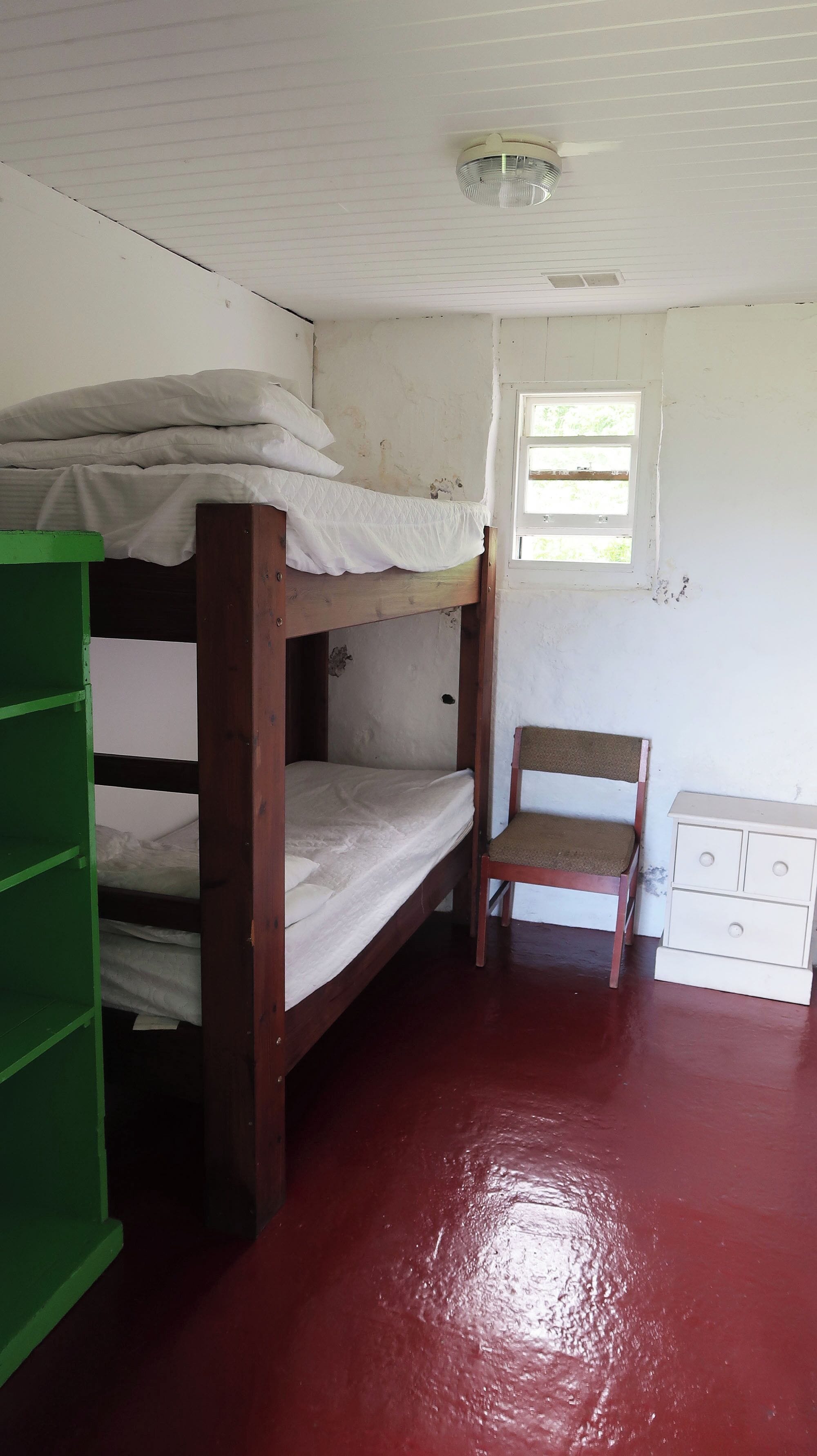 Une chambre de dortoir avec des lits superposés, une chaise, une petite commode et une fenêtre.