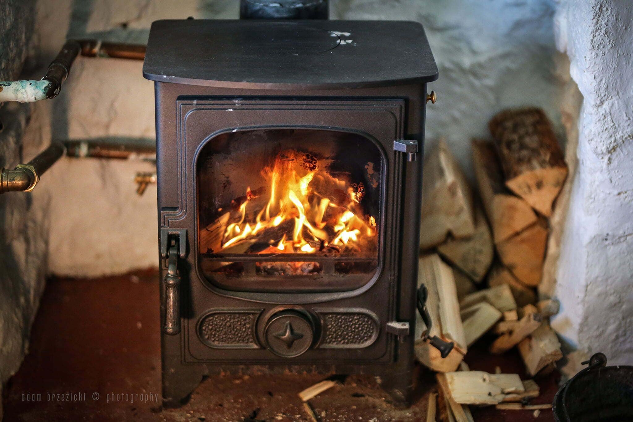 A wood-burning stove with visible flames, a metal handle, and a door with a star-shaped lock.