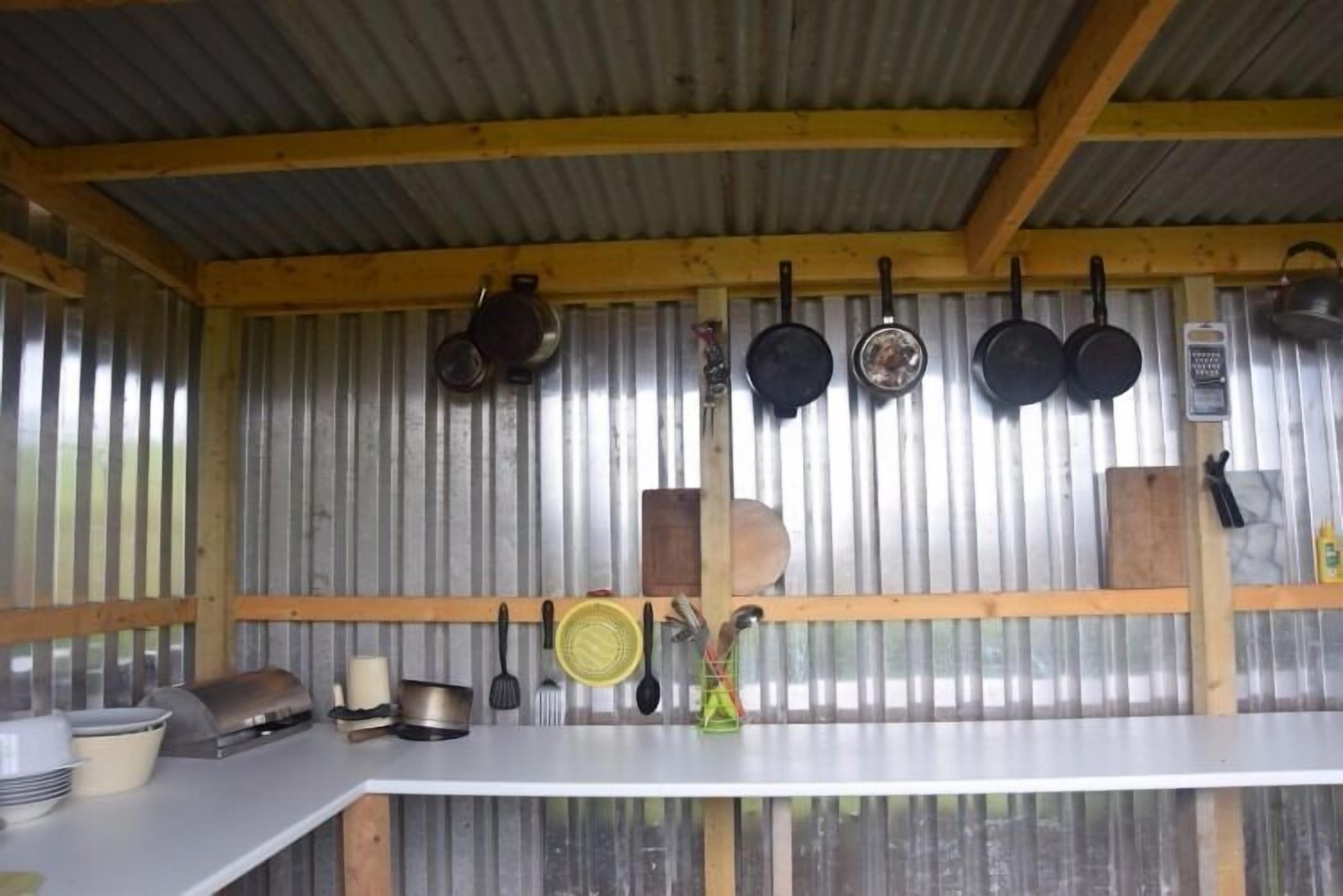 A rustic kitchen with a corrugated metal wall, wooden beams, and various kitchen utensils and cookware hanging on the wall.