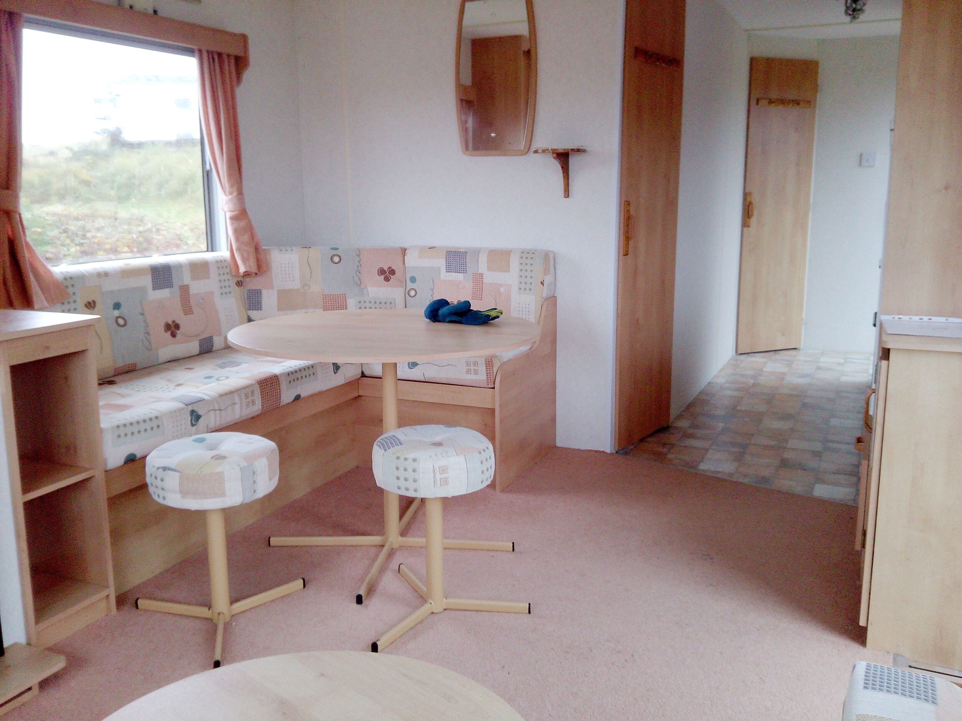 A compact kitchen with a round table, two stools, a bench with a patterned cushion, and a window with curtains.