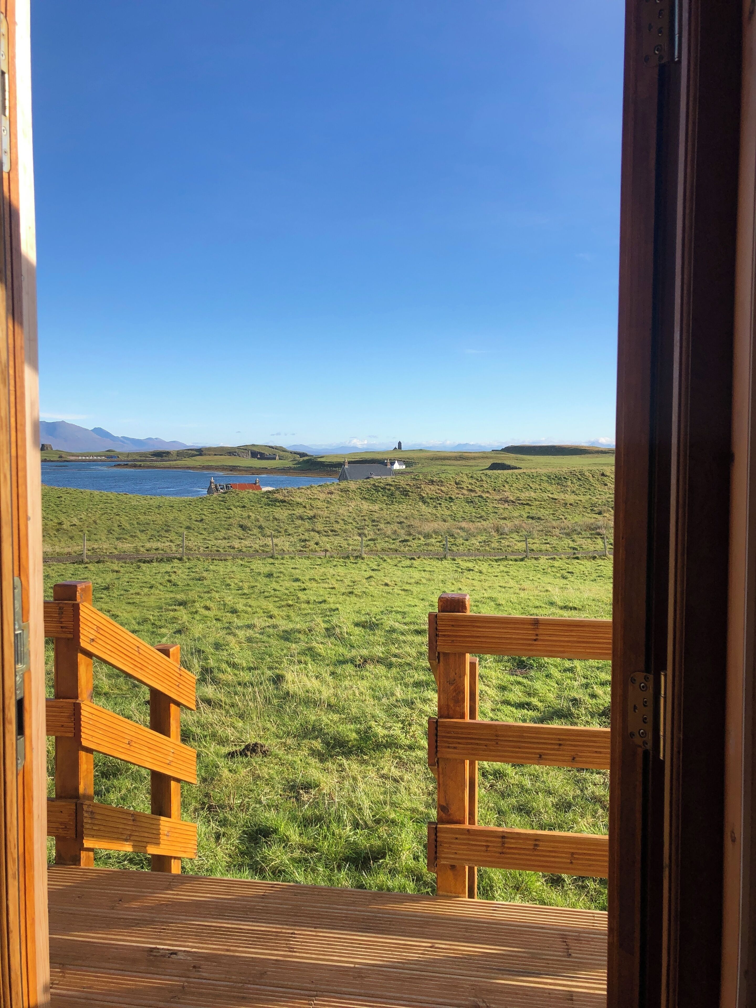En træterrasse der fører ud til en græsplæne med frit udsyn til vand og fjerne bjerge.