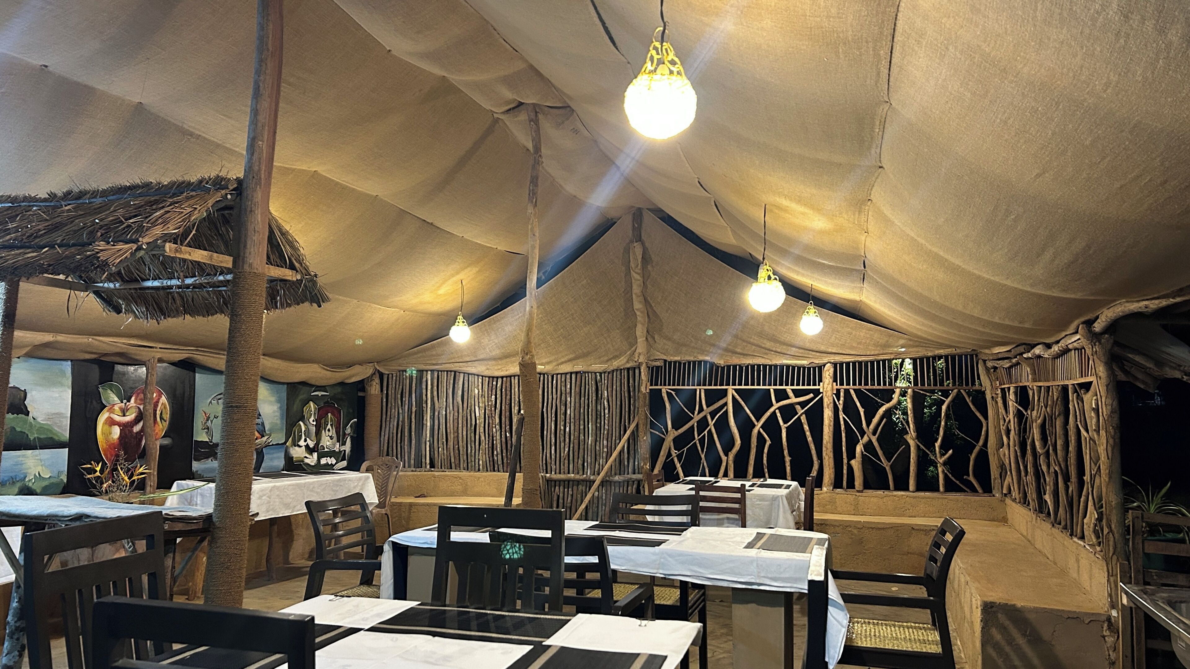 Un espace de restauration intérieur avec des tables et des chaises, un toit de chaume et des luminaires suspendus.