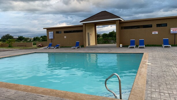 Piscina con sedie blu e zona coperta, circondata da un vialetto in mattoni.