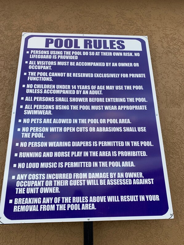 A sign listing pool rules, including no pets, no open cuts, and no loud music.