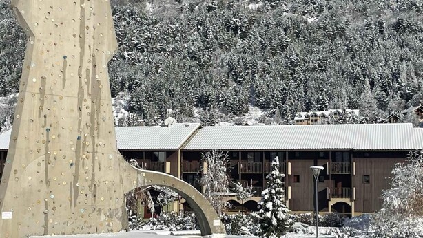 A building with a snow-covered landscape, a large climbing wall, and a wooden structure with multiple balconies. - 250m from ski slopes, terrace, tv, 24m², Serre Chevalier (La Salle-les-Alpes)