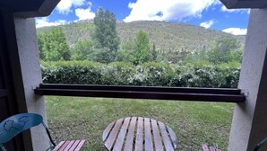 A balcony with a wooden table and two chairs, overlooking a grassy area and a forested hill. - 250m from ski slopes, terrace, tv, 24m², Serre Chevalier (La Salle-les-Alpes)