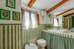 A bathroom with striped green and white tiles, a white sink, a toilet, and a mirror. - La Maisonette - Casa Vacanze (Laconi)
