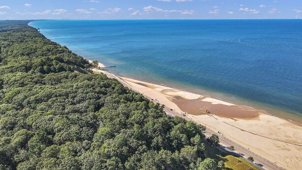Vista aèria d'una platja, amb vegetació abundant d'un costat i un mar blau i translúcid de l'altre.