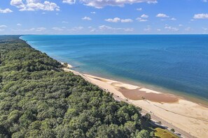 Une vue aérienne d’une plage, avec une végétation luxuriante d’un côté et une mer bleue et limpide de l’autre.