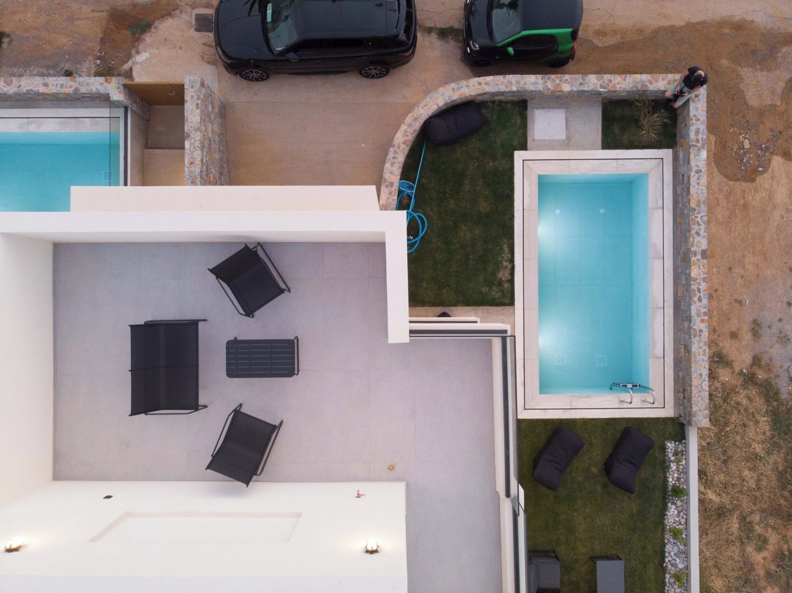 An aerial view of a property with two swimming pools, a covered patio area with seating, and a small garden.