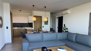 A modern living room with a grey sectional sofa, a wooden coffee table, and a dining area with a kitchen in the background. - Destino Luxury Villas Gournes (Hersonissos)