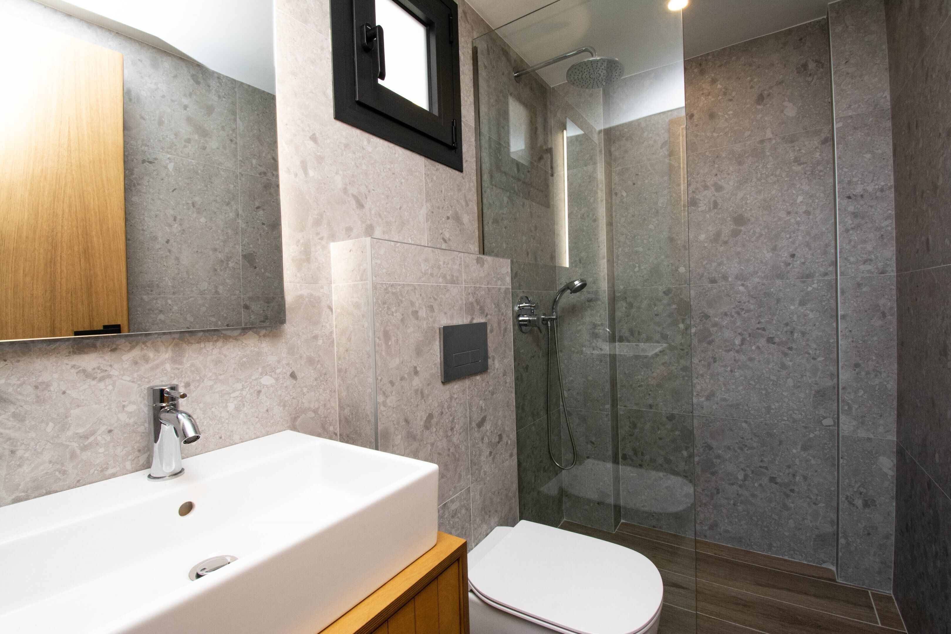 A modern bathroom with a large white sink, a toilet, and a glass-enclosed shower area.