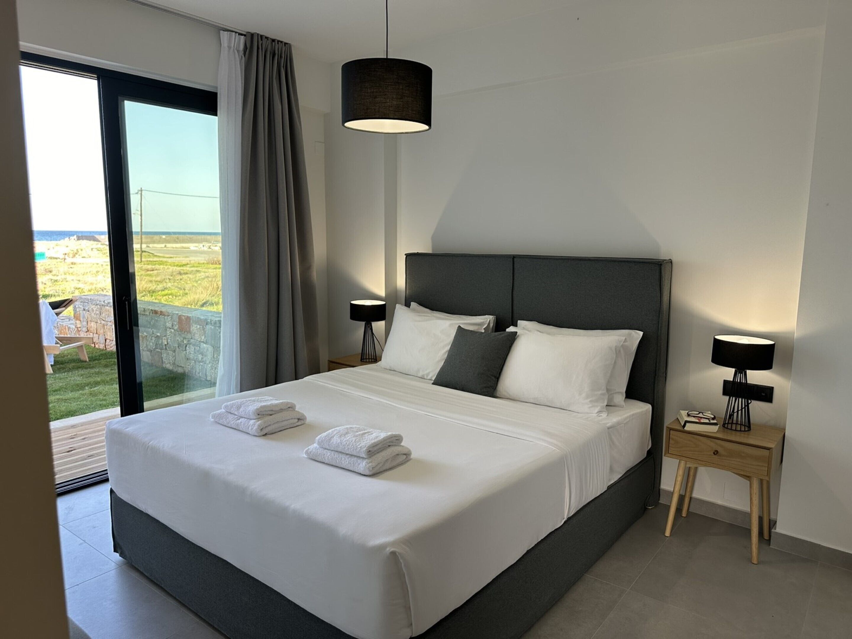 Una habitación de hotel moderna con una cama grande, dos mesitas de noche con lámparas y vistas al exterior.