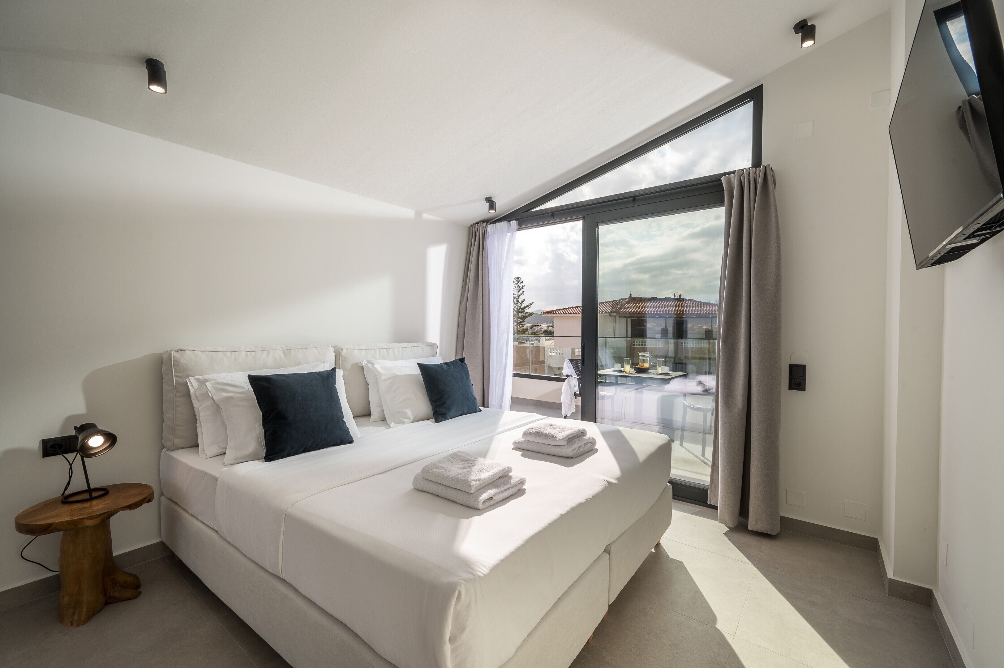A modern hotel room with a large bed, a bedside table with a lamp, and a view of the outside balcony.
