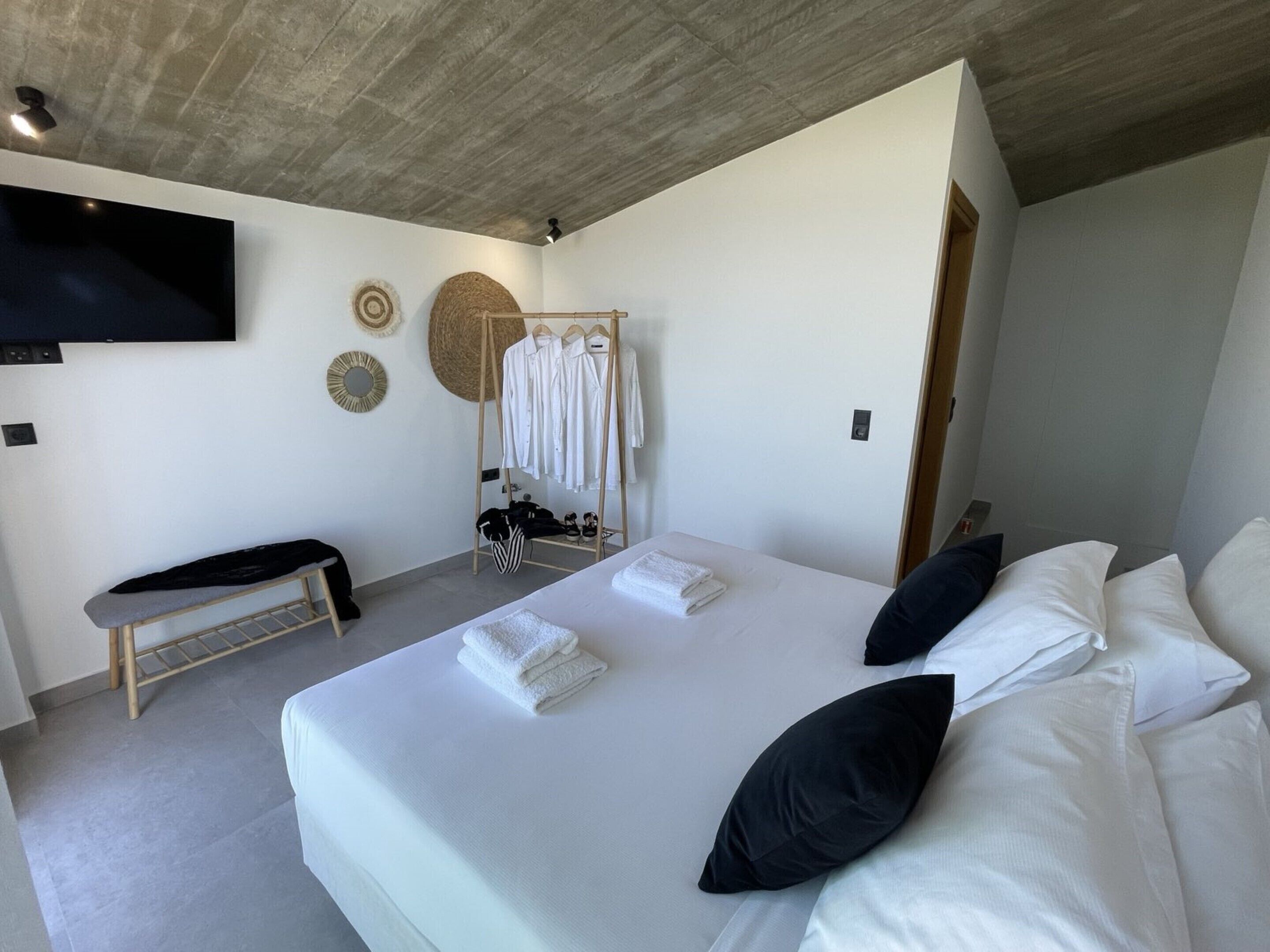 Un dormitorio moderno con una cama grande, un banco, un perchero y un televisor de pantalla plana en la pared.