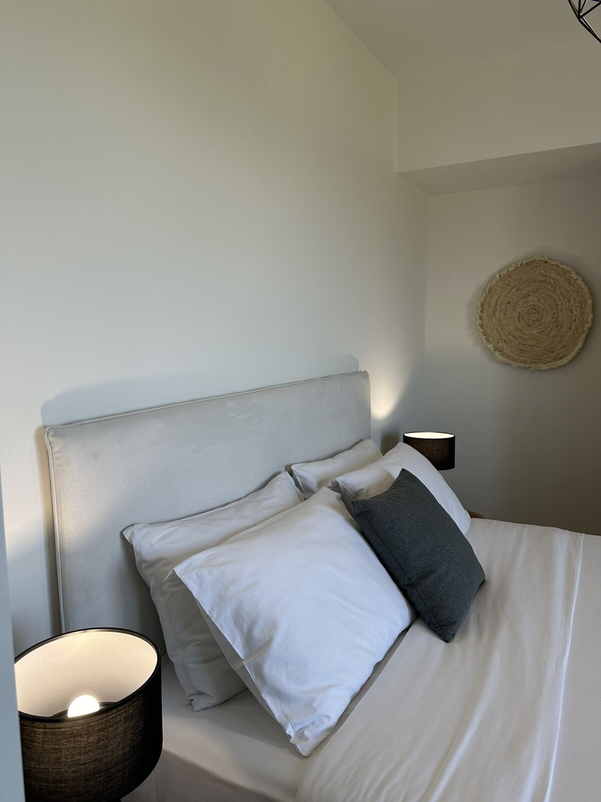 A neatly made bed with a headboard, a bedside lamp, and a woven wall hanging.