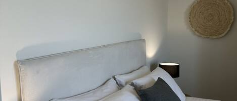 A neatly made bed with a headboard, a bedside lamp, and a woven wall hanging.