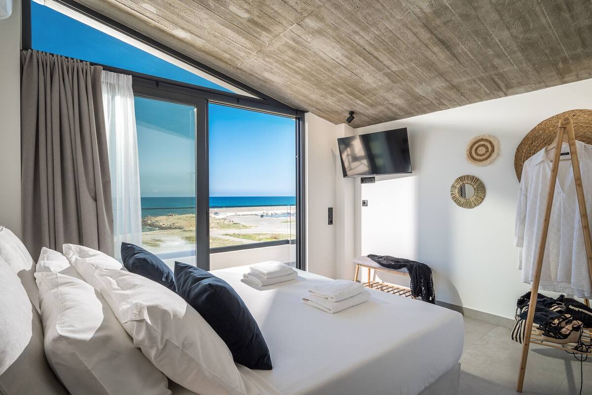 A modern hotel room with a large bed, a TV, and a view of the beach.