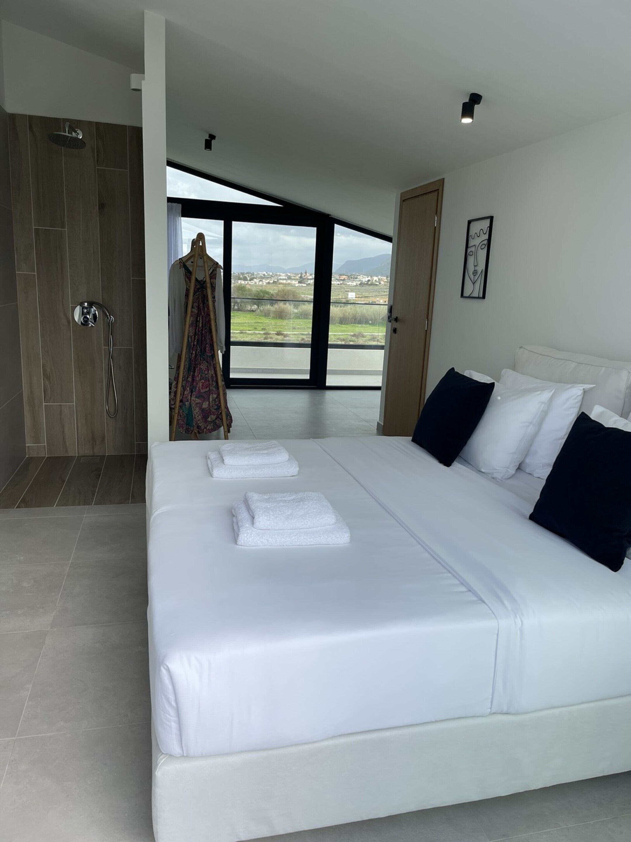 A modern bedroom with a large bed, white linens, and a view of the countryside through a glass door.