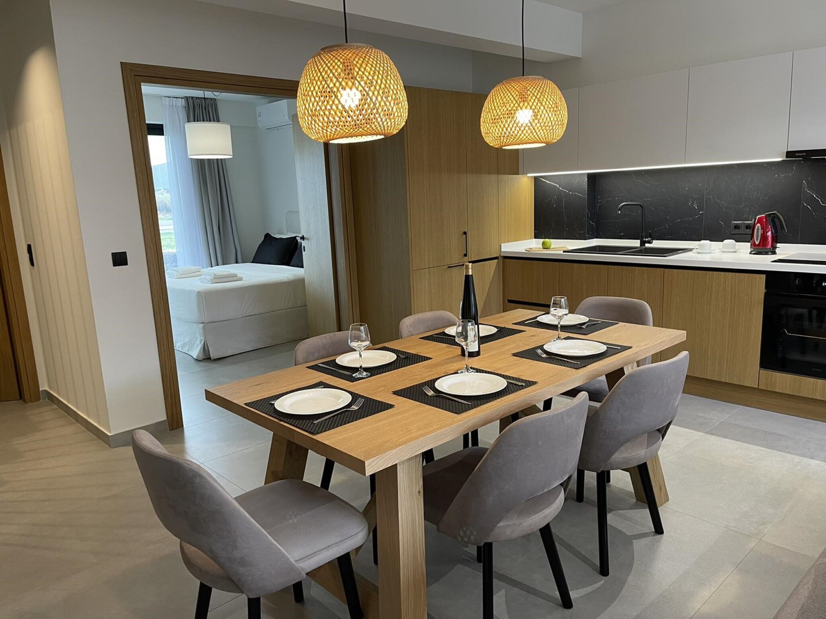 A modern dining area with a wooden table set for four, grey upholstered chairs, and two woven pendant lights.