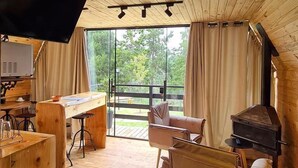 Ein gemütliches Blockhauskaminzimmer mit Holzbalkendecke, einem großen Fernseher, einem Klavier, einer Couch und einem Kamin.