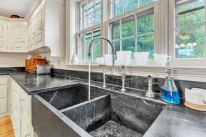 A kitchen with a black marble countertop, white cabinets, and a window with a view of trees. - 18th century 3-bedroom renovated farmhouse in peaceful Whately with WiFi, AC (Whately)