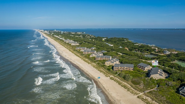 An aerial view of a coastal residential area with beachfront properties, including multi-story buildings and individual houses, along a sandy beach with ocean waves. - 4 BDR, Ocean Front Condo (Lucky Enough) in Ocean Grove Complex (Salter Path)