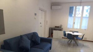 Ein Wohnzimmer mit blauem Sofa, einem Esstisch mit Stühlen und einer kleinen Küchenzeile.