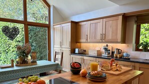 Cozinha moderna com armários de madeira, bancada para refeições rápidas e vista para o verde lá fora.