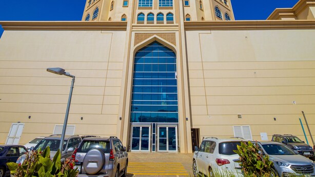 A tall building with a central entrance featuring large glass doors, surrounded by parked cars and greenery. - NIAMEY MALL & RESIDENCE (Niamey)